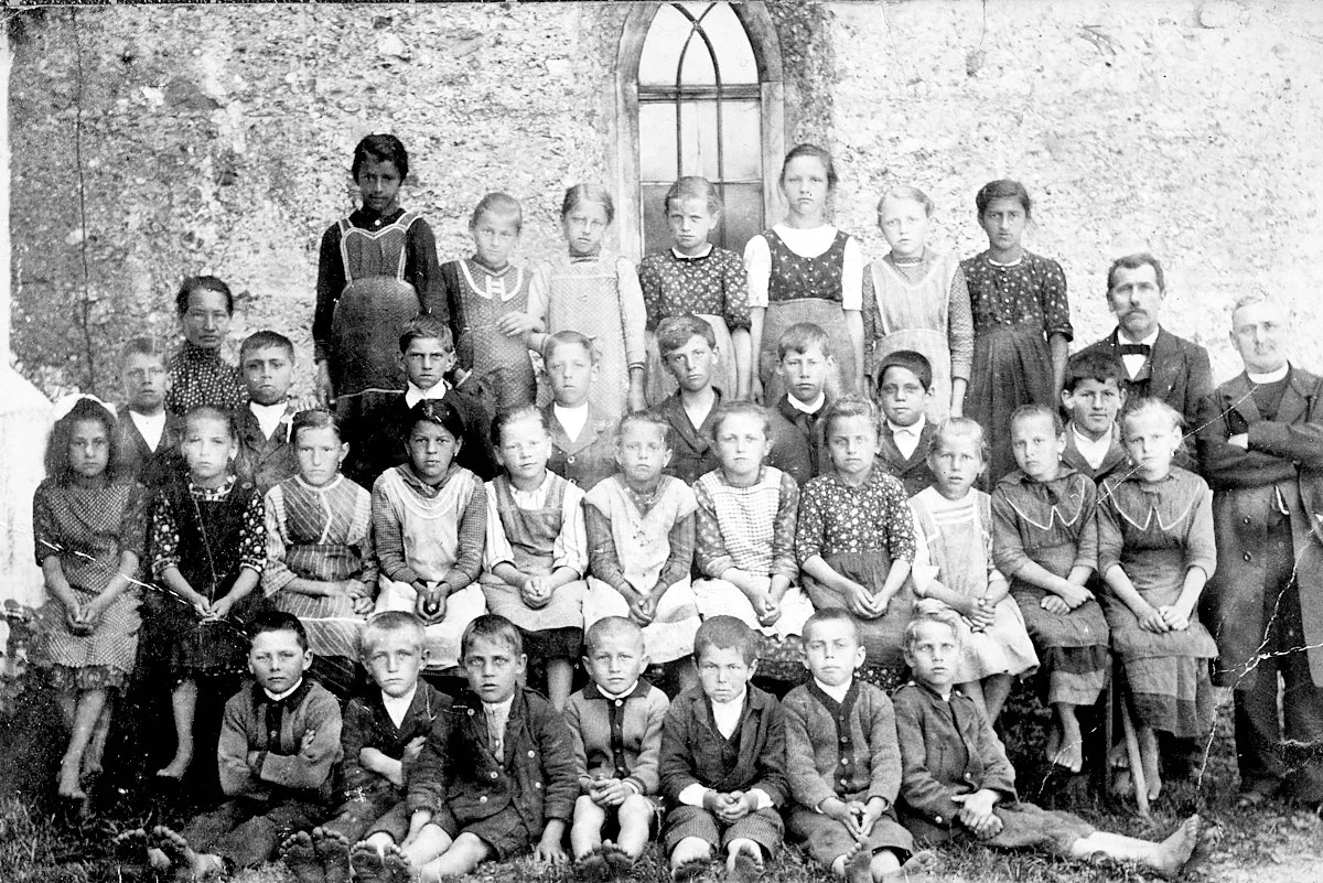 Historische Klassenfotografie einer Schulklasse vor einer Kapelle